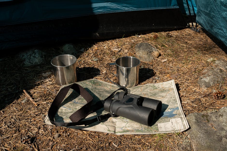 Close-up of camping gear, including binoculars, map, and cups outside a tent.