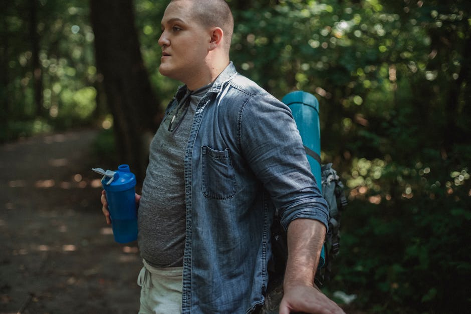 Side view of serious traveler with backpack standing with bottle of water in hand and resting in forest in daytime